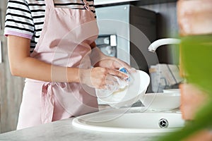 Woman washing dishes in kitchen sink, closeup view.