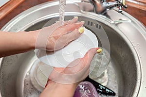 Woman washing dishes in kitchen sink, closeup view. Cleaning chores