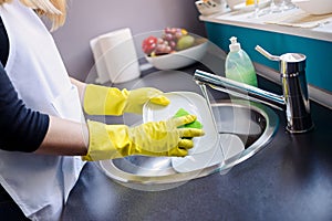 Woman washing dishes in the kitchen with sponge.