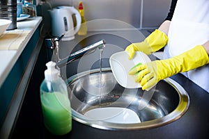 Woman washing dishes in the kitchen with sponge.