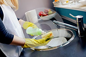 Woman washing dishes in the kitchen with sponge.