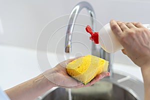 Woman washing dishware, pouring soap at sponge, standing on kitchen