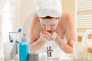 Woman washing face above bathroom sink