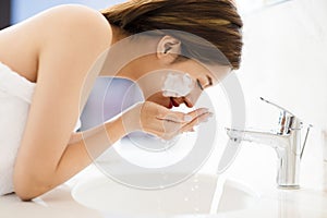 Woman washing face with clean water in bathroom
