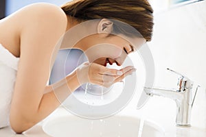 Woman washing face with clean water in bathroom