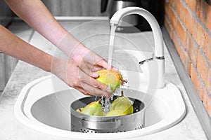 Woman washing fresh ripe pears in kitchen sink