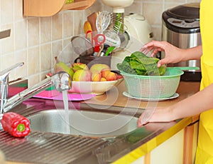 Woman washing fresh vegetables in kitchen