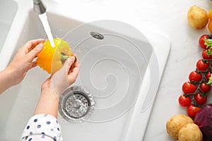 Woman washing fresh yellow bell pepper in kitchen sink, top view