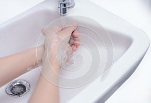 Woman washing hand with soap foam and tap water in bathroom. Hand clean under faucet on sink for personal hygiene to prevent flu