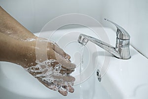 Woman washing hands under the water tap in bathroom with using soap gel for cleaning and prevention inflection coronavirus