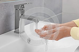 Woman washing hands with water from tap in bathroom, closeup