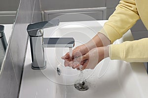 Woman washing hands with water from tap in bathroom, closeup