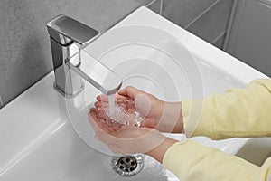 Woman washing hands with water from tap in bathroom, closeup