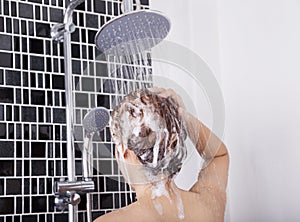 Woman washing head and hair in the rain shower by shampoo, rear