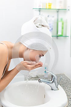 Woman washing her face with water above bathroom.
