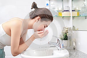 Woman washing her face with water above bathroom sink.