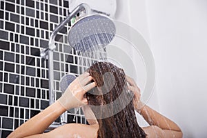 Woman is washing her hair and face by rain shower, rear view