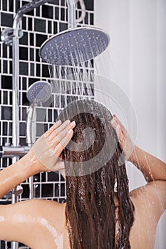 Woman is washing her hair and face by rain shower, rear view