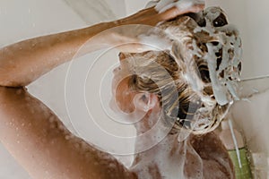Woman is washing her hair with a shampoo while taking shower
