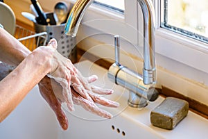 A woman is washing her hands with soap at the kitchen sink.
