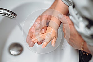 woman washing little baby boys hands. Hygiene and disinfection of hands at home with soap and tap water