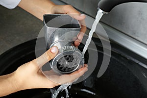 Woman washing manual meat grinder under tap water in kitchen sink indoors, closeup