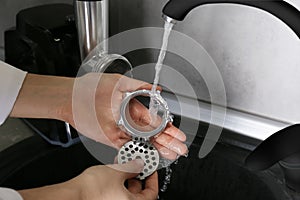 Woman washing parts of electric meat grinder under tap water in kitchen sink indoors, closeup