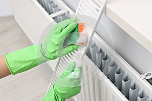 Woman washing radiator grill with sponge and detergent indoors, closeup