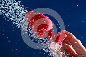 Woman washing red anal plug under shower on blue background.