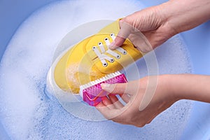 Woman washing shoe with brush in basin, closeup