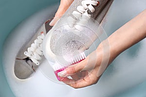 Woman washing shoe with brush in basin