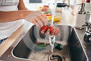 Woman washing tomatoes in kitchen sink close up.