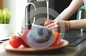 Woman washing tomatoes in kitchen sink close up