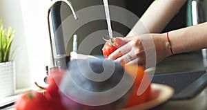 Woman washing tomatoes in kitchen sink close up
