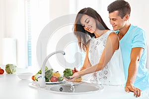 Woman washing vegetables, man hugging her in kitchen