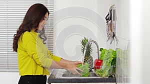 Woman washing vegetables in the sink in the kitchen at home
