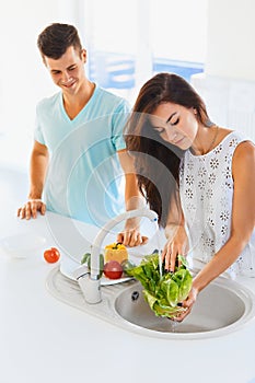 Woman washing vegetables in the sink and man standing next to he
