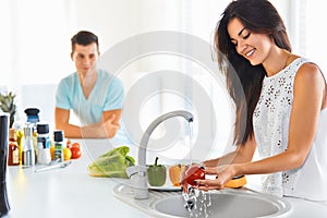 Woman washing vegetables in the sink and man standing next to he