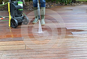Woman washing wooden terrace with high pressure water