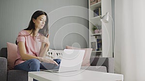 Woman watch news using looking at home laptop sitting on sofa. Young housewife girl checking social networks screen feed
