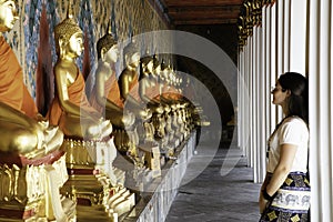 Woman watching aligned golden buddha statues in the Emerald Temple at Bangkok