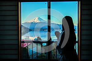 Woman are watching Fuji moutain outside the window while holding a cup of tea in the morning.