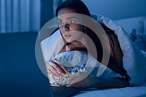 Woman watching movie and eating popcorn at night