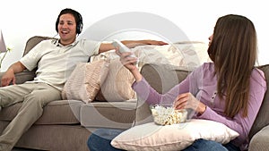 Woman watching tv with popcorn while her husband listens to music