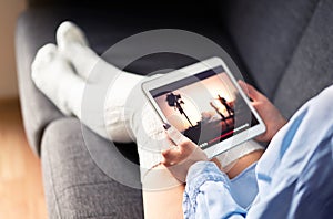 Woman watching tv series or movie stream with tablet on couch wearing cozy long socks. Girl streaming film with mobile device.