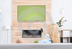 Woman watching TV on sofa in room with decorative fireplace