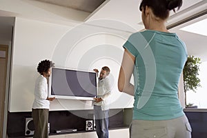 Woman Watching Two Men Moving Plasma Television