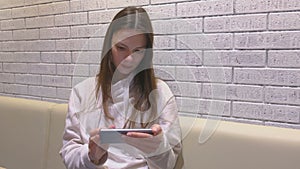 Woman is watching a video on mobile phone sitting and waiting somebody in cafe.