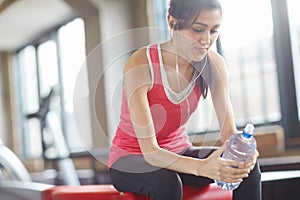 Woman, water bottle and earphones in gym for workout, fitness and exercise for wellness. Training, energy and female