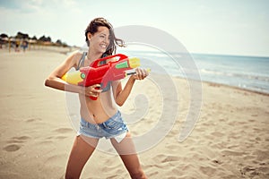 Woman with water guns have fun on the beach by the sea